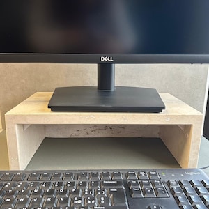 Op de afbeelding: Een beige stenen monitorstandaard met een zwarte Dell-monitor erop. Op de voorgrond een zwart toetsenbord met het Logitech-logo.