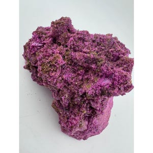May include: A rough, porous rock specimen featuring a vibrant magenta and deep purple coloration. The surface is highly textured with irregular, jagged protrusions and small crevices, displaying a crystalline, mineral-like appearance throughout.