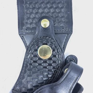 Peut inclure: Gros plan sur un &eacute;tui en cuir noir avec un motif de tissage et des rivets de couleur laiton. L'&eacute;tui poss&egrave;de une boucle et un rabat, et est con&ccedil;u pour contenir un objet. Le cuir semble robuste et bien travaill&eacute;.