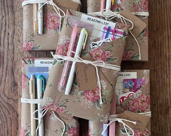 May include: Five rectangular packages wrapped in brown floral paper, each tied with white string and a brown tag labeled Romance. Each package includes a reading list card, colorful pens, sticky note tabs, and a decorative bookmark tucked inside.