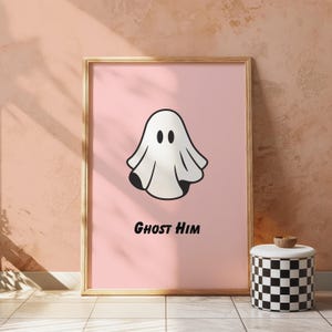 Puede incluir: Un póster rosa enmarcado con una ilustración de fantasma de dibujos animados y el texto "Ghost Him" en negro. El fantasma es blanco con detalles negros. Un taburete a cuadros blanco y negro está a la derecha del póster.