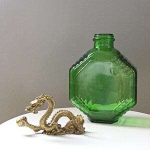 May include: A gold-colored dragon figurine sits on a white surface next to a green glass bottle with a faceted design.