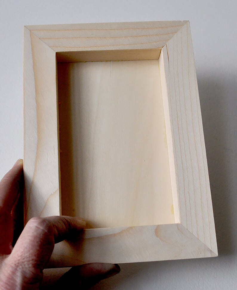 May include: A plain wooden frame with a light wood finish. The frame is empty and ready to be used for a picture or other artwork.