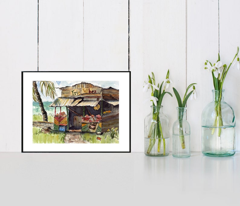 May include: A watercolor painting of a small wooden shack with a sign that reads "Irie Vibes". The shack is surrounded by lush greenery and a palm tree. The painting is framed in black.