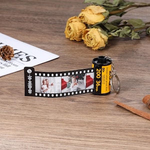 May include: A black and yellow film canister keychain with a 35mm colour print film label. The keychain has a silver metal ring and a black and white photo strip attached. The photo strip has two photos of children.