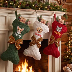 May include: Three bone-shaped Christmas stockings in green, white, and red cable knit fabric. Each stocking features a pet portrait, a name embroidered in script, and a brown polka-dot bow. The names Penny, Sunny, and Buddy are displayed.