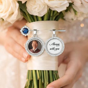 May include: Two silver round pendants with a photo and the text "Always with you" are displayed. The pendants are surrounded by clear crystals. A blue gemstone ring and a bouquet of white flowers are also visible.
