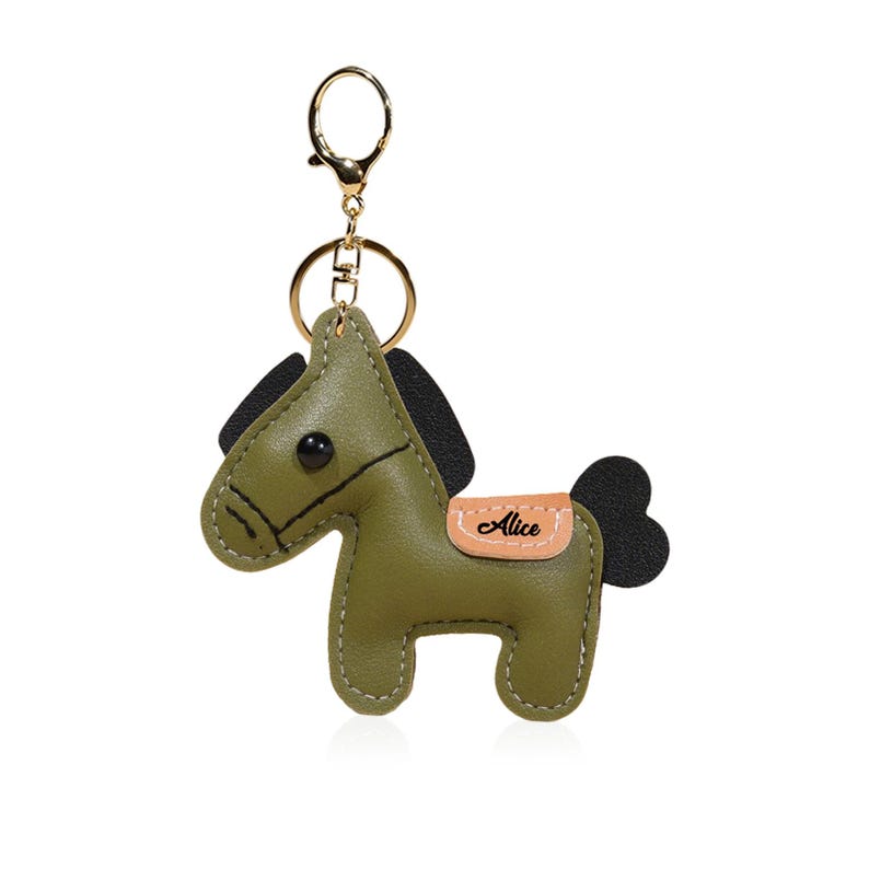 May include: Olive green leather horse keychain with black mane and tail. Features a gold-tone keyring and a small tan saddle with the name "Alice". The horse has a stitched design and a button eye.