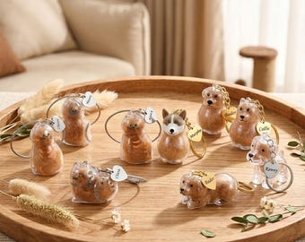May include: A collection of clear resin keychains shaped like cats and dogs, each with a small gold-colored tag. The keychains are displayed on a wooden tray, with some featuring personalized names.