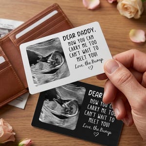 Puede incluir: Dos tarjetas rectangulares con imágenes de ultrasonido y el texto "DEAR DADDY, NOW YOU CAN CARRY ME TOO CAN'T WAIT TO MEET YOU! Love, the Bump". Una tarjeta es blanca, la otra negra. Una cartera de cuero marrón en el fondo.