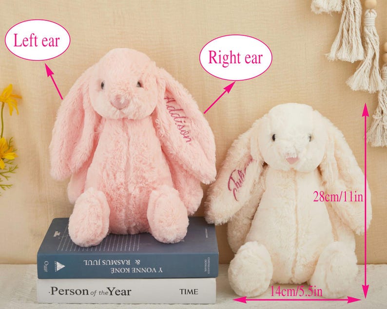K&ouml;nnte beinhalten: Zwei Pl&uuml;schhasen, einer rosa und einer cremefarben, werden gezeigt. Der rosa Hase hat "Addison" auf dem Ohr gestickt. Der cremefarbene Hase ist 28 cm hoch und 14 cm breit, mit "Tilly" auf dem Ohr gestickt.