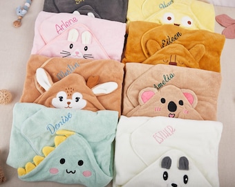 Peut inclure: Une collection de serviettes à capuche pour bébés de différentes couleurs, chacune avec un motif de visage d'animal. Les serviettes sont brodées de noms tels que "Arlene", "Martin" et "Denise". Les motifs incluent un lapin, un koala et un dinosaure.