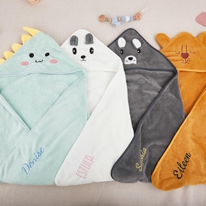 May include: Four hooded baby towels in pastel colors. The towels are shaped like animals: a dinosaur, a bear, a husky, and a lion. Each towel has a name embroidered on it. The dinosaur towel is light green, the bear towel is white, the husky towel is gray, and the lion towel is orange.