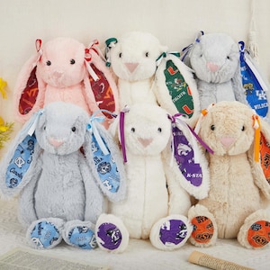 Puede incluir: Una colección de conejos de peluche en varios colores, cada uno con orejas estampadas y lazos. Los conejos tienen diferentes logotipos de equipos en sus orejas y pies, incluidos logotipos de equipos universitarios.