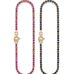 May include: Two tennis bracelets with gold settings and circular clasps. One bracelet features a continuous row of vibrant pink round-cut stones, while the other bracelet features a continuous row of deep black round-cut stones in a matching design.