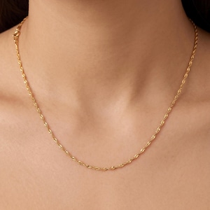 Puede incluir: Un collar de cadena de oro fino tipo cuerda con un diseño de eslabones trenzados y texturizados. La cadena metálica descansa alrededor del cuello, presentando un acabado pulido que refleja la luz a lo largo de su patrón continuo de eslabones dorados.