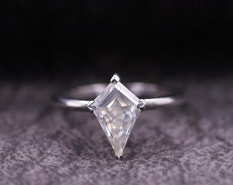 May include: A silver-toned ring featuring a single kite-shaped gemstone set in a prong setting. The band is thin and smooth, supporting the geometric stone which is positioned vertically at the center of the ring's circular metal band.