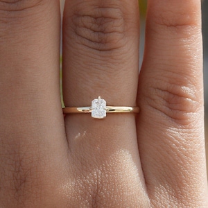 Puede incluir: Un anillo de banda de oro simple con un pequeño diamante de forma rectangular.
