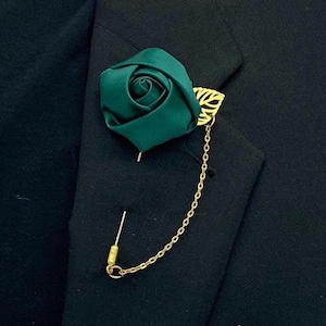 May include: A dark green fabric rose with a gold leaf design and a gold chain attached to a pin.