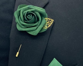 May include: A dark green fabric rose with a gold leaf accent and a gold pin. The rose is pinned to a dark suit jacket. A matching dark green pocket square is in the pocket of the jacket.