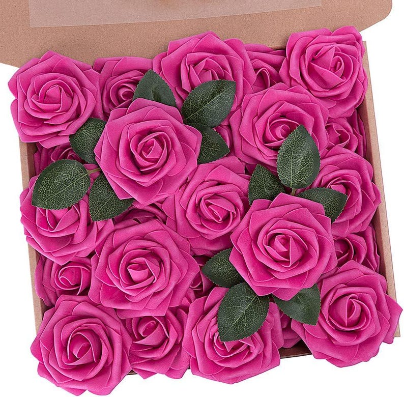 以下が含まれることがあります： ピンクの人工バラの花の頭でいっぱいの箱。バラは円形に配置され、茎は外側を向いています。バラは鮮やかなピンク色で、リアルな外観をしています。