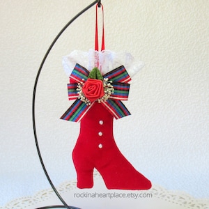 May include: Red velvet boot Christmas ornament with a plaid bow, white lace trim, and a red rose.