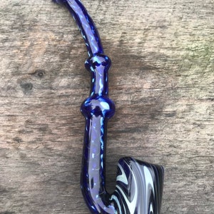 May include: A blue glass pipe with a curved stem and a bowl. The pipe has a dark blue color with white and light blue swirls in the bowl. The stem has a textured design.