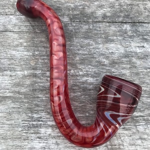 Peut inclure: Une pipe en verre rouge et blanc avec une tige incurvée et un bol. La pipe a un motif en spirale.