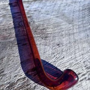 May include: A deep red glass pipe with a long, curved stem. The pipe is made of clear glass with a red tint.
