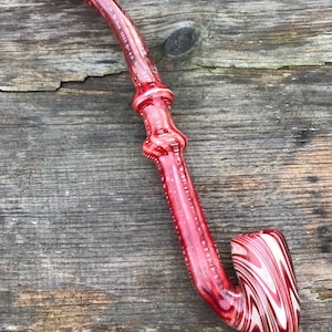 Könnte beinhalten: Eine rote und weiße Glaspfeife mit einem gebogenen Schaft und einem Kopf. Die Pfeife hat ein Wirbelmuster und ist aus klarem Glas mit roten und weißen Akzenten gefertigt.