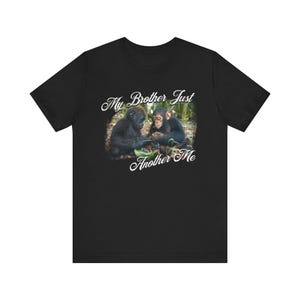 Könnte beinhalten: Schwarzes T-Shirt mit einer Grafik von zwei Schimpansen in einer natürlichen Umgebung. Der Text "My Brother Just Another Me" ist in kursiver Schrift über und unter dem Bild angeordnet. Das T-Shirt besteht aus einem weichen Material.