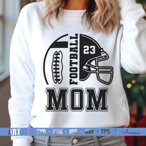 May include: White sweatshirt with a black graphic design featuring a football, helmet, and the text "FOOTBALL MOM" with the number 23. The design is centered on the front of the shirt.