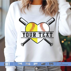 Puede incluir: Sudadera blanca con un diseño de softball. El softball tiene forma de corazón y está formado por dos mitades de un softball. Dos bates de béisbol cruzados están detrás del softball. El texto "YOUR TEXT" está en una pancarta negra debajo del softball.