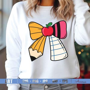 May include: A white sweatshirt with a yellow, pink, and blue bow with a red apple in the center. The bow is made to look like a pencil and a piece of notebook paper.