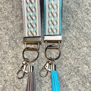 May include: Two keychains with silver metal rings and blue and gray tassels. The keychains have a woven design with white, blue, and gray stripes.