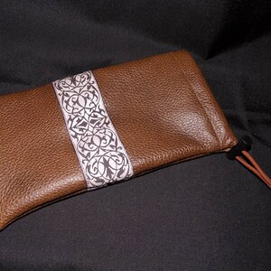 May include: A brown leather pouch with a white and brown patterned trim and a drawstring closure.