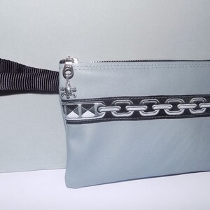 May include: A gray zippered pouch with a black chain design and a black strap. The pouch has a silver skull charm attached to the zipper.