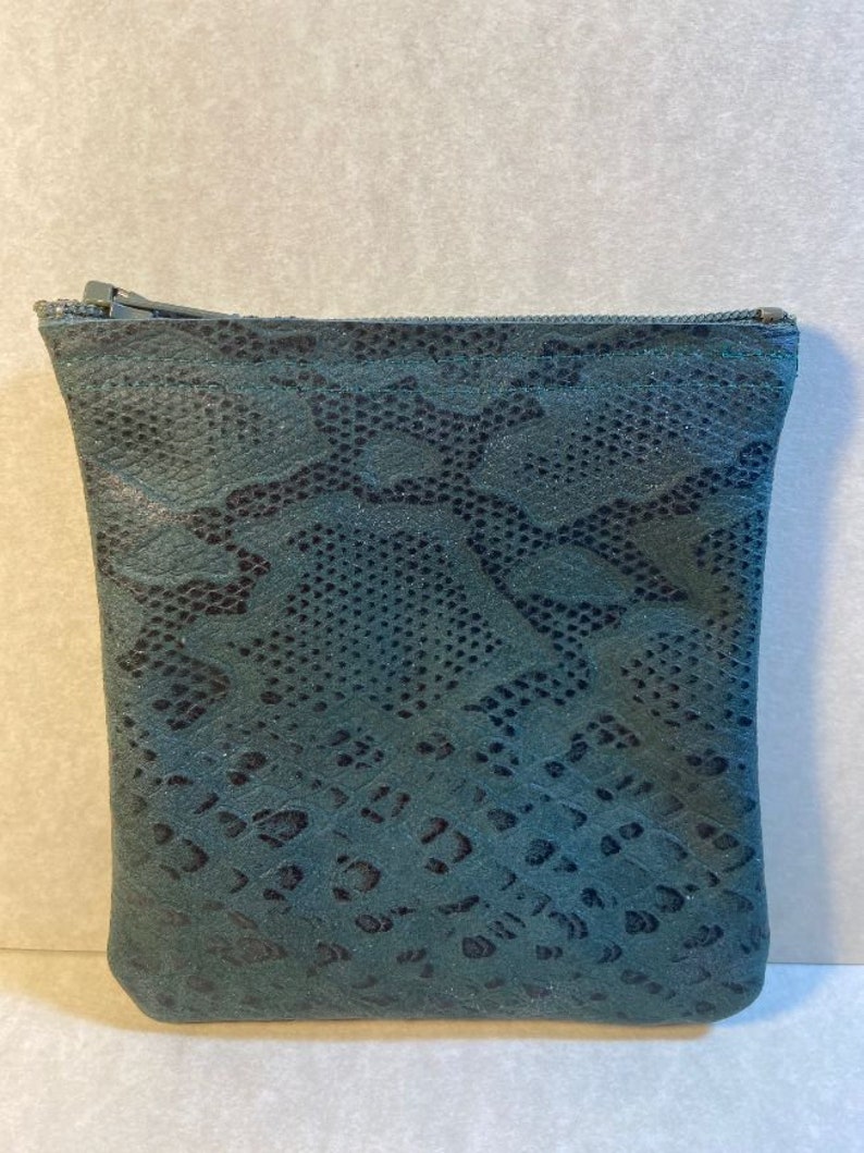 Puede incluir: Una peque&ntilde;a bolsa verde oscuro con cremallera y estampado de piel de serpiente.