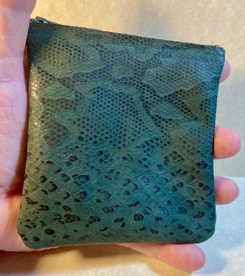 Puede incluir: Una peque&ntilde;a bolsa verde con cremallera y estampado de piel de serpiente.