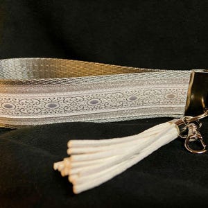 May include: A silver and white patterned key chain with a white tassel. The key chain has a silver metal clasp and a silver ring.