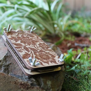 May include: A wooden box with a floral design and metal clasps. The box is closed and sitting on a rock.