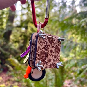 May include: A wooden key holder with a floral design and metal clasps. The holder is attached to a red carabiner.