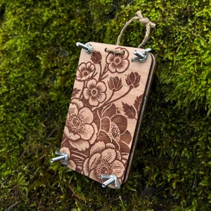 May include: A wooden floral print block with metal clamps, used for printing on fabric or paper.
