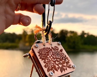 Puede incluir: Un llavero de madera con un diseño floral. El llavero está unido a un mosquetón plateado.