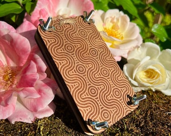 May include: A wooden flower press with a geometric pattern, featuring four metal bolts and a twine loop. The press is surrounded by pink and white roses, with green foliage in the background.