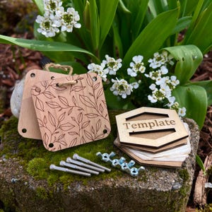 May include: A wooden template with the word "Template" engraved on it, along with a set of screws and nuts. The template is surrounded by green foliage and white flowers.