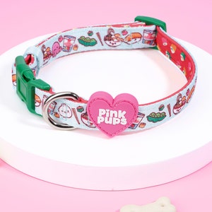 Peut inclure: Un collier pour chien bleu et rouge avec un charme en forme de cœur rose qui dit "Pink Pups". Le collier présente un motif de divers aliments japonais, notamment des sushis, des ramen et des edamames.