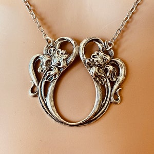 Pode incluir: Um colar de prata com um grande pingente adornado com um design floral estilizado. O pingente tem a forma de um círculo com dois motivos florais de cada lado.