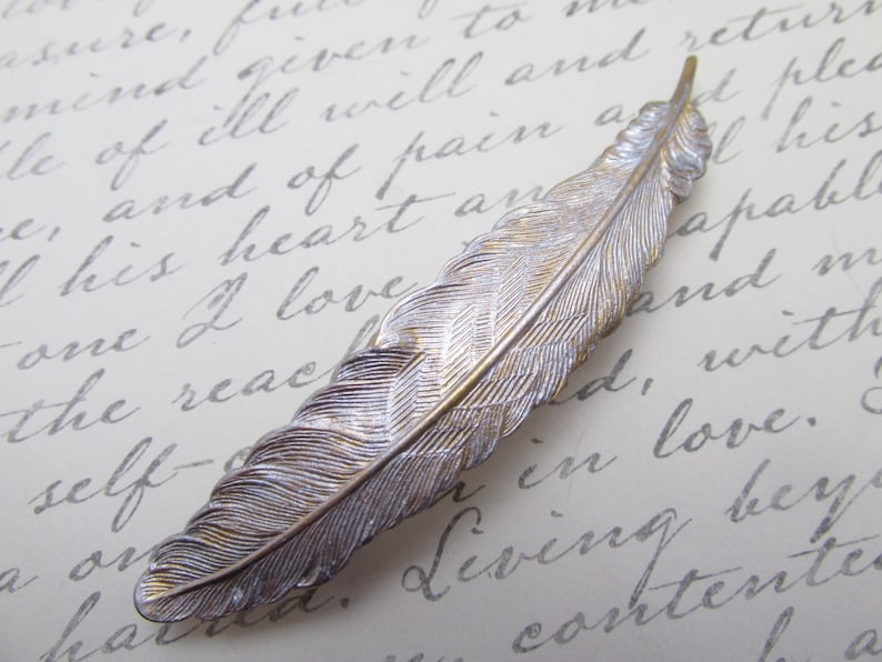 May include: A silver and gold feather-shaped hair clip. The feather has a detailed design and is a delicate accessory.