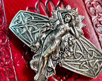 May include: Silver-toned metal barrette featuring a reclining female figure with flowing hair and floral accents. The barrette has intricate Celtic knotwork and is set against a textured red background. A decorative hair accessory.
